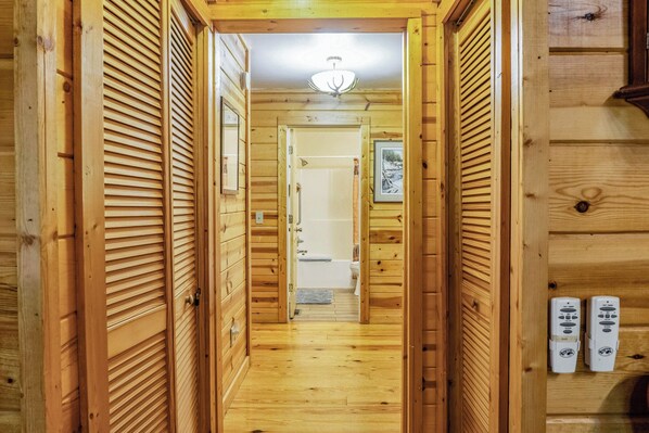 Un pasillo de madera con una lámpara en el techo, puertas de madera y vistas a un baño con bañera e inodoro.