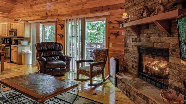 A cozy cabin interior with a fireplace, wooden walls, a dining area, and a kitchen. - Jake's Hideaway (ellijay)