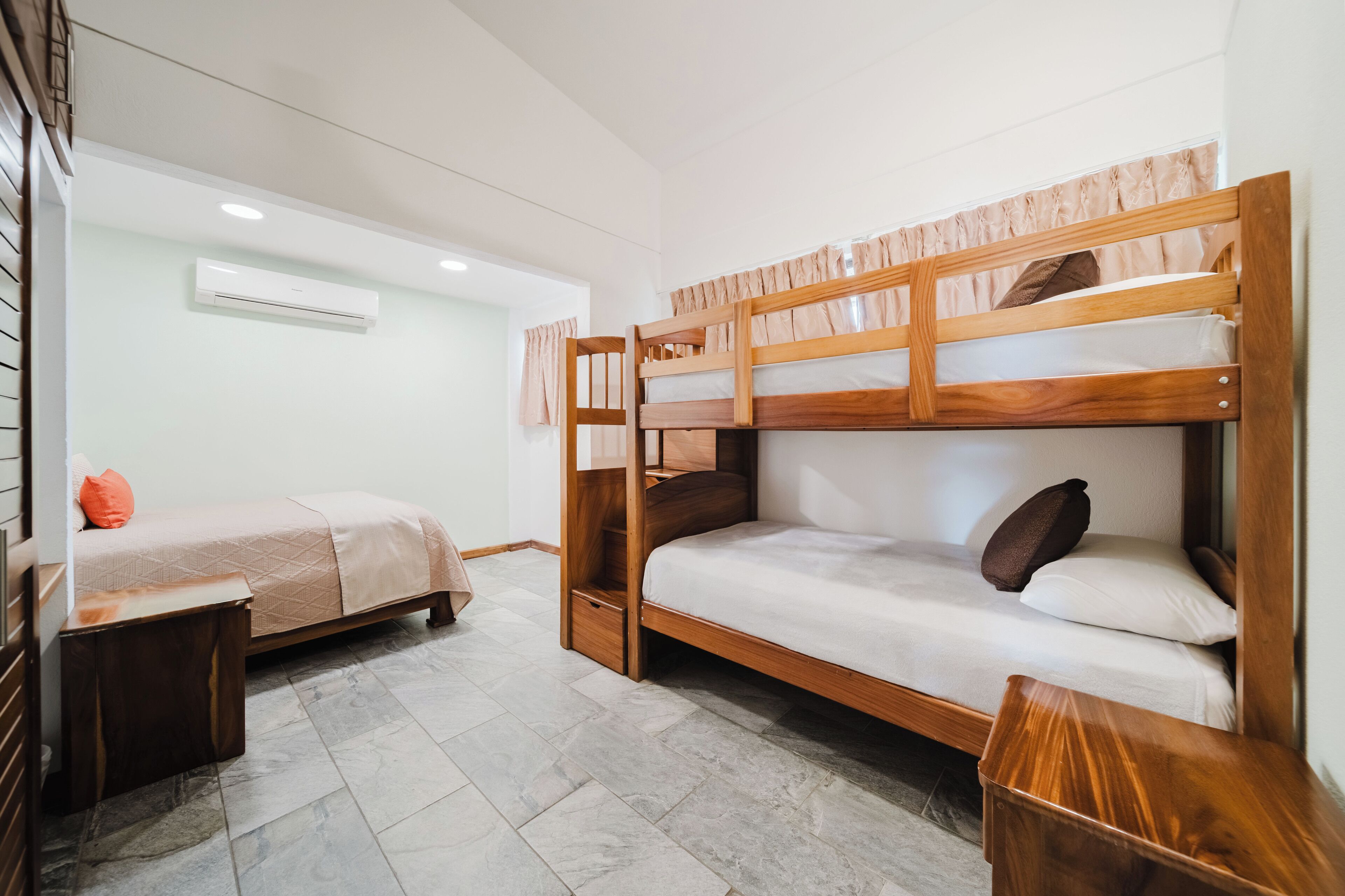 Habitación con literas de madera, una cama individual con almohada, una mesita de noche y una pequeña mesa de madera.