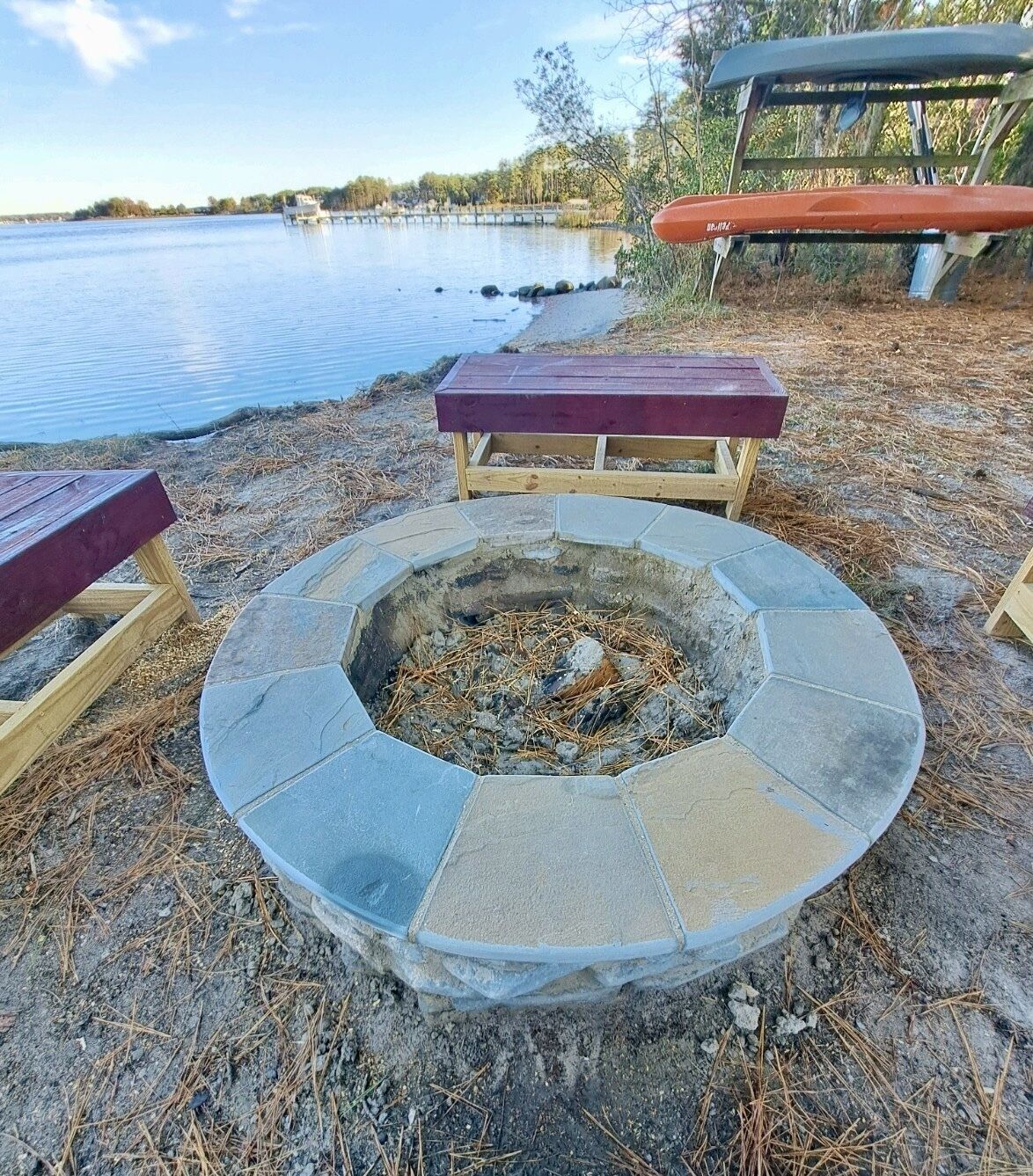 Ein Steinkamin inmitten von Holzbanken, mit einem See im Hintergrund.