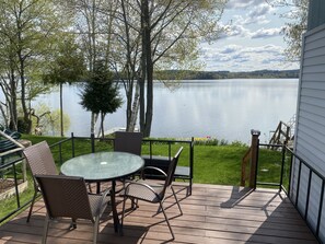 A deck with a glass table and chairs, overlooking a lake with trees and a grassy area. - Waterfront home on the lake shore of Beautiful Lake Memphremagog, Newport, VT. (Newport)