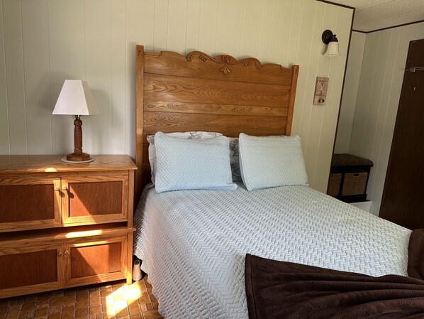 A neatly made bed with a wooden headboard, a bedside table with a lamp, and a wooden cabinet. - Waterfront home on the lake shore of Beautiful Lake Memphremagog, Newport, VT. (Newport)