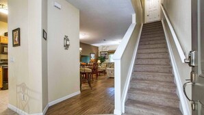 A home interior with a staircase leading to a second floor, a dining area with wooden flooring, and a kitchen in the background. - Oakwater - Spacious 3BR 2.5BA townhome, gated (Kissimmee)