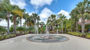 A circular fountain with water jets in the center, surrounded by palm trees and a paved walkway. - Oakwater - Spacious 3BR 2.5BA townhome, gated (Kissimmee)