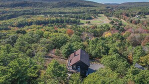 A wooden cabin surrounded by dense forest, with a clear view of the surrounding hills and a golf course in the distance.