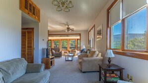 A spacious living room with a high ceiling, large windows, and a view of the outdoors.
