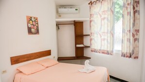 A neatly arranged bedroom with a single bed, a wooden headboard, a wall-mounted air conditioner, a shelf unit, and a window with patterned curtains. - 2 Blocks from ADO station + free bikes (Tulum)