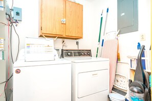 A laundry room with a washing machine, dryer, wooden cabinet, and various cleaning tools. - What Time Is It? - Quaint 3 BR Home - Check in any day! (Surf City)
