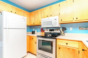 A compact kitchen with wooden cabinets, a white refrigerator, a microwave, a stove, and a small oven. - What Time Is It? - Quaint 3 BR Home - Check in any day! (Surf City)