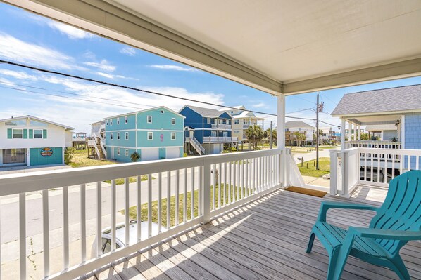 A covered porch with a view of a beachfront community, including houses with balconies and a beachside restaurant. - What Time Is It? - Quaint 3 BR Home - Check in any day! (Surf City)