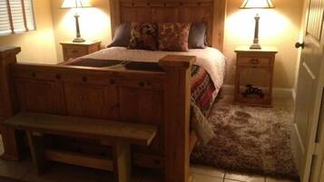 A bedroom with a wooden bed, two bedside tables with lamps, a bench at the foot of the bed, and a door.