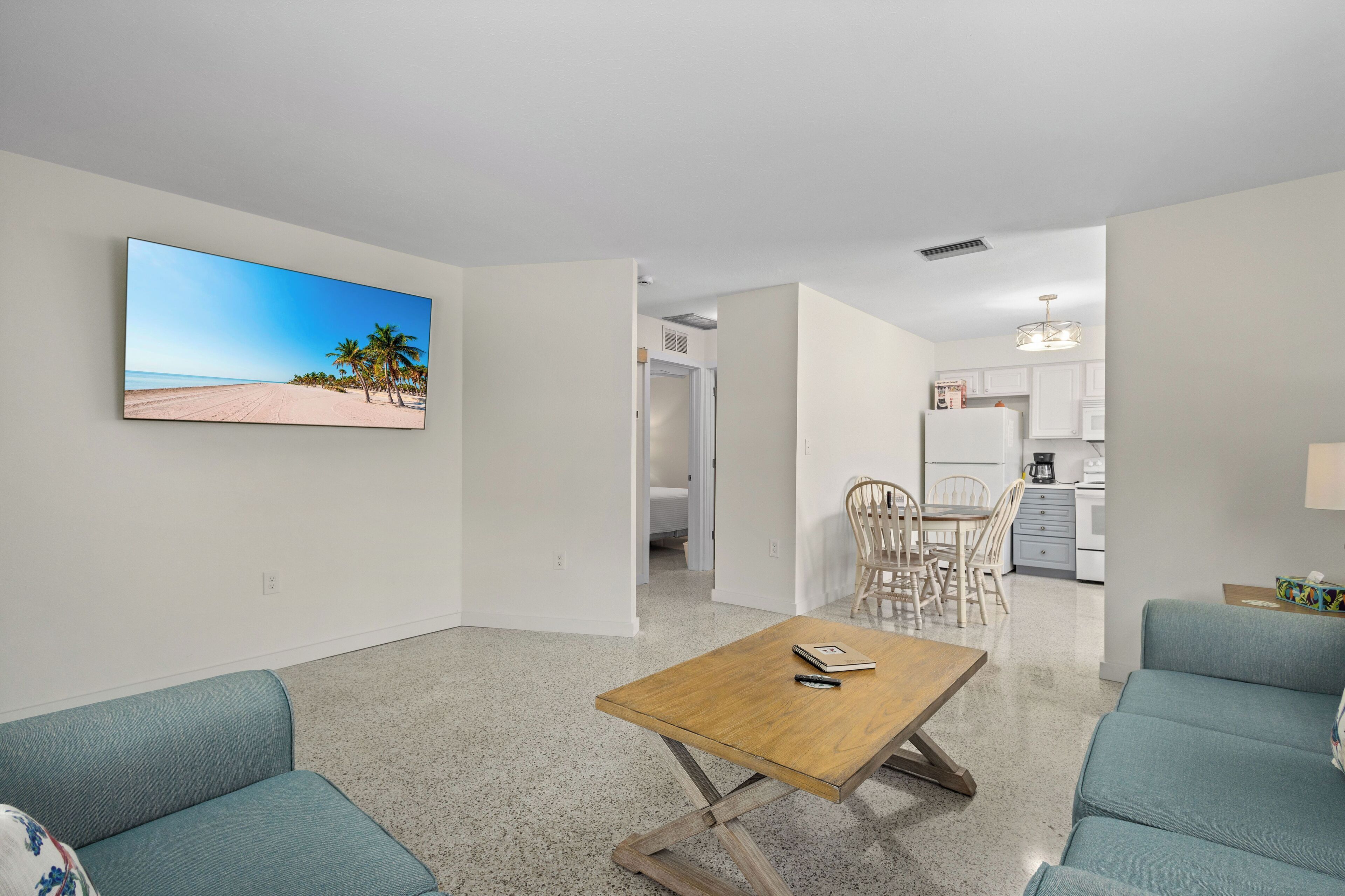 A modern living room with a wooden coffee table, teal sofas, and a large beach-themed painting on the wall.