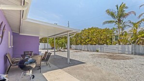 Un patio techado con una parrilla, asientos exteriores y vista a palmeras.
