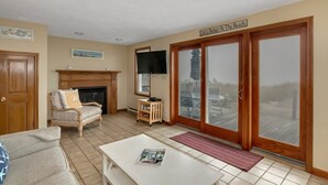 A living room with a fireplace, a television, and a sliding glass door leading to a deck. - Waterfront cottage with private beach in Sandwich! 179B North Shore Blvd (Sandwich)