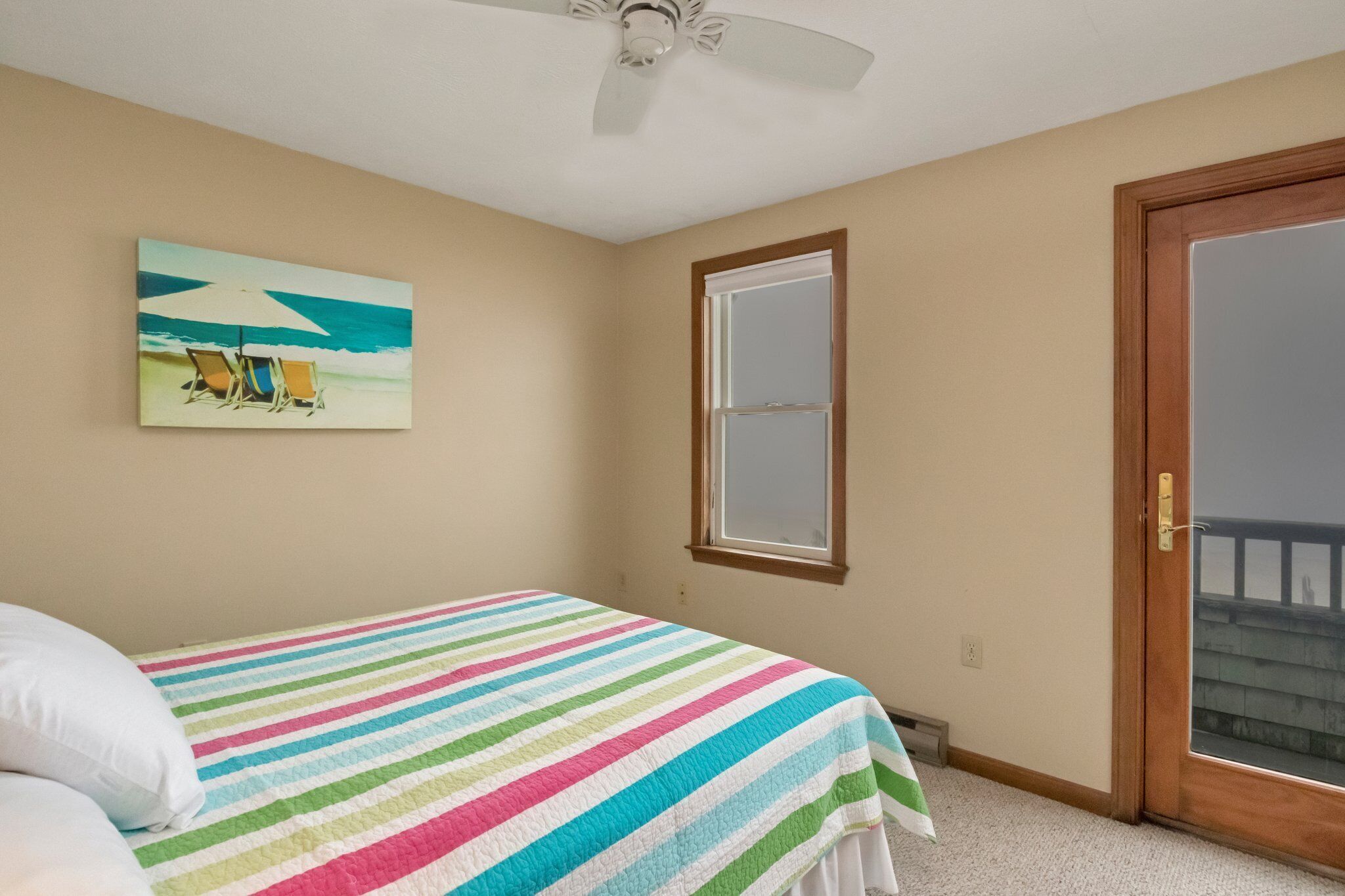 A bedroom with a bed, a ceiling fan, a window, and a door leading to a balcony.