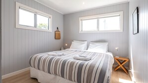 A bedroom with a bed, two bedside tables, a hanging basket, and two windows. - THE WAIHEKE PAD | Be My Guest (Oneroa)