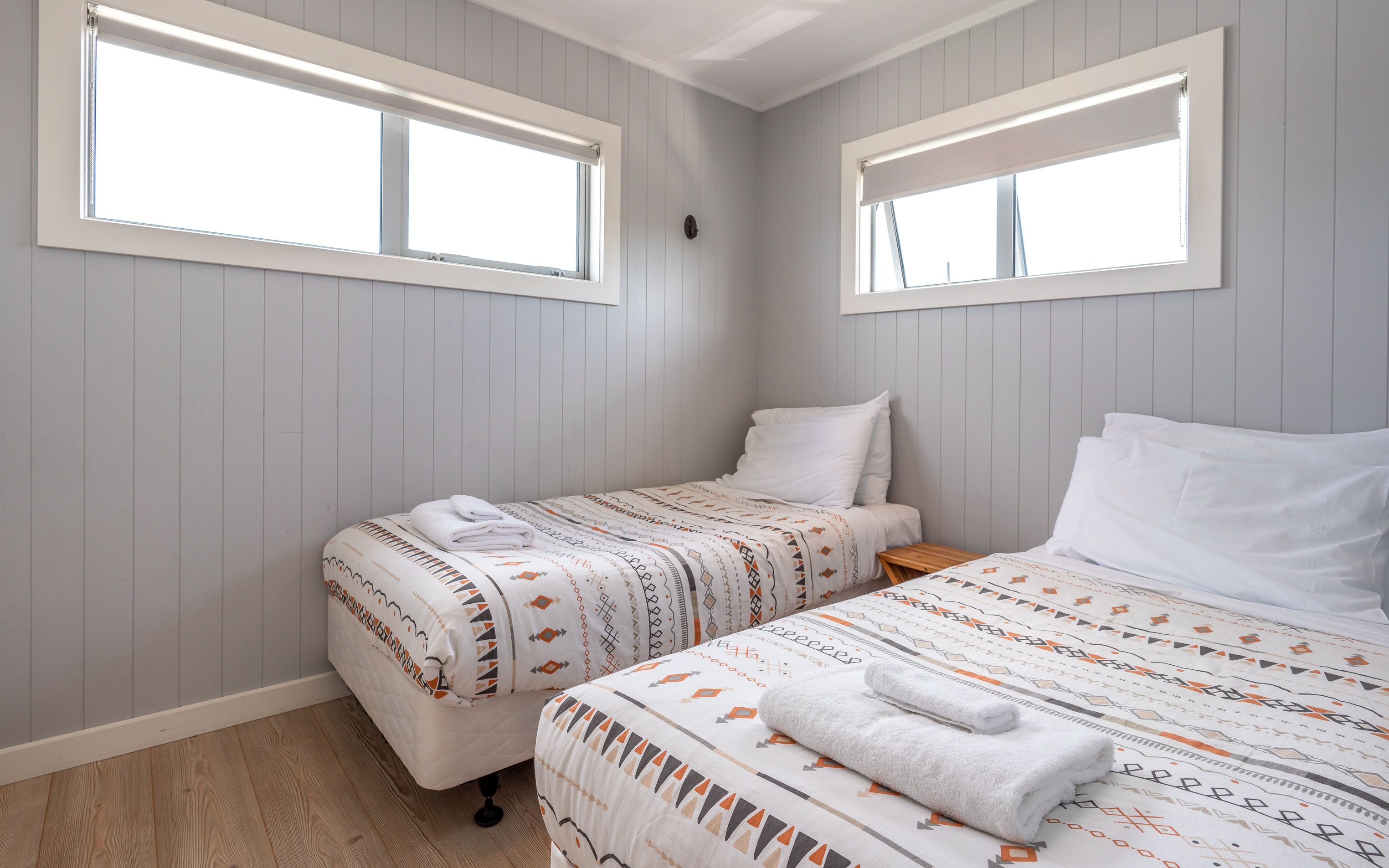 Un dormitorio con dos camas, piso de madera y paredes de color claro.