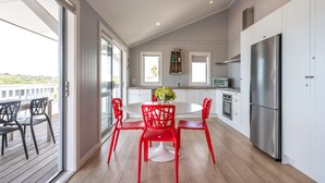 A modern kitchen with white cabinets, a stainless steel refrigerator, and a dining area with a round table and red chairs. - THE WAIHEKE PAD | Be My Guest (Oneroa)