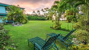 A lush garden with a lawn, two metal chairs, and a table.