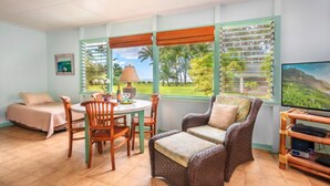 A room with a bed, a dining table with chairs, a sofa, a TV, and large windows with blinds.