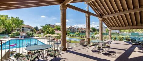 An outdoor pool area with a covered patio, tables, and chairs.