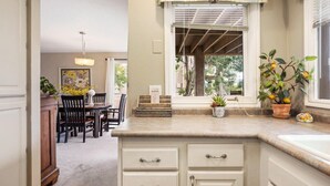 A kitchen with a dining area, featuring a window with blinds, a hanging light fixture, and various kitchen appliances. - Peaceful Sports Village Retreat | Beautiful Mountain Views, Pools & Patio (St George)