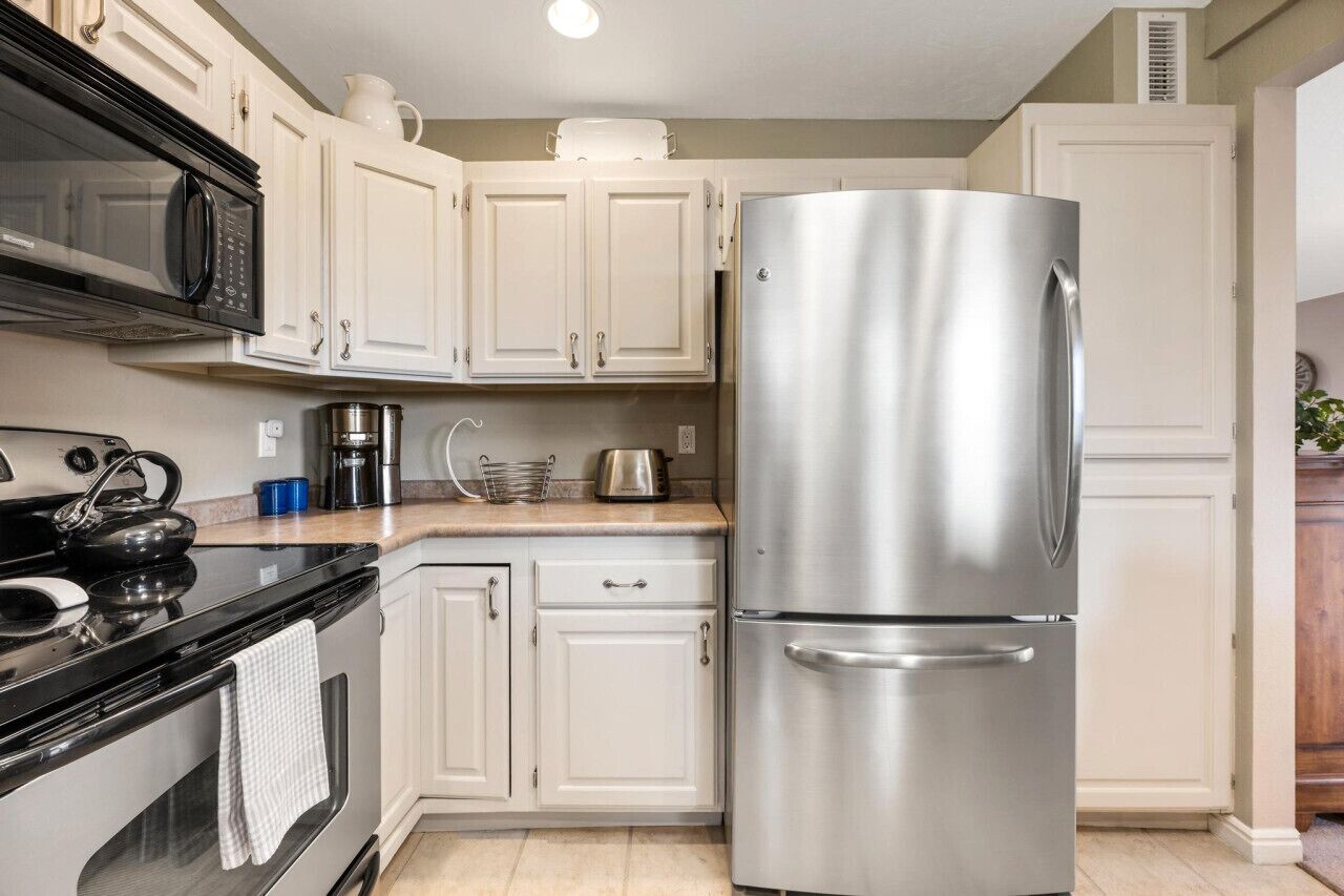 A kitchen with white cabinets, a stainless steel refrigerator, a black stove, and a microwave.