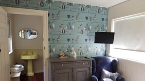 A bedroom with a bed, a dresser, a chair, a TV mounted on the wall, and a bathroom with a sink and mirror. - THE STABLE WILLYUNG WA (Willyung)