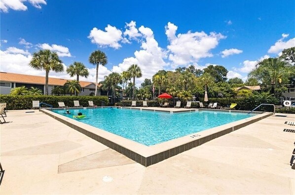 Relax by the pool surrounded by palm trees and lounge chairs with umbrellas.