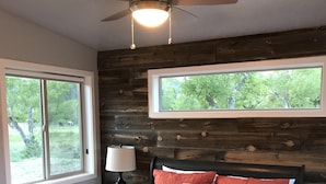 Ein Schlafzimmer mit einem Bett, einem Deckenventilator, einem Fenster und einem Nachttisch.