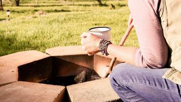 Una persona sentada junto a una fogata improvisada al aire libre, sosteniendo una taza.