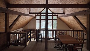 A spacious attic room with a high ceiling, wooden beams, a large window, and a dining table with benches. - Ski-in Ski-out Killington Chalet on Great Eastern Trail, Huge Loft + 4 Bedrooms (Killington)