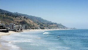 A coastal beach with buildings on a hillside, a sandy shore, and the ocean. - Oceanfront Retreat on Sandy Carbon Beach - Dolphin (Malibu)