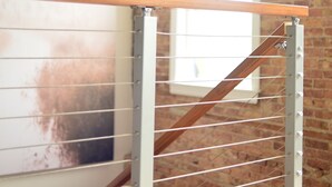 Una escalera con barandilla de madera y balaustrada de metal, que conduce a una habitación con pared de ladrillo y ventana.