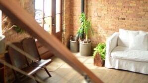 Una habitación con paredes de ladrillo visto, un sofá blanco, suelo de madera y una lámpara colgante.