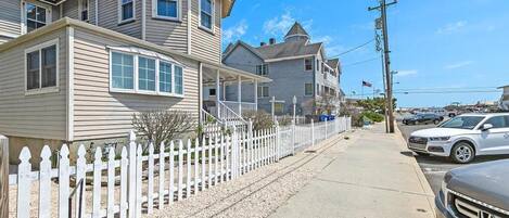 A two-story house with a white picket fence, a driveway, and parked cars.