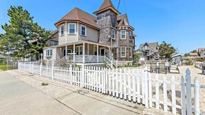 A large, two-story house with a stone tower, a white picket fence, and a front porch.