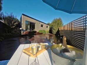 Une terrasse extérieure avec une table dressée pour un repas, comprenant un verre de vin, un bol de glace et un plateau en bois avec de la nourriture.
