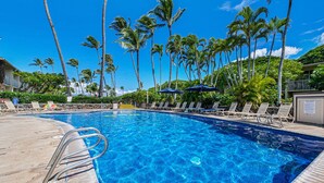 A clear blue pool surrounded by lounge chairs and palm trees, with a wooden deck and a lifeguard stand.