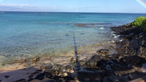 A beach with clear water, rocks, and a rainbow.