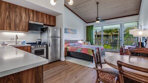 A modern kitchen with wooden cabinets, stainless steel appliances, and a large island. There is a bedroom with a bed and a view of the outdoors.