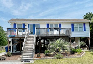 A two-story house with a balcony, a covered porch, and a small staircase leading to the entrance. - Prior Engagement: Pet Friendly Beach Cottage at Emerald Isle on The Point (Emerald Isle)