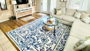 A living room with a wooden wall, a flat-screen TV, a white entertainment unit, a patterned rug, a glass coffee table, and a striped sofa. - Prior Engagement: Pet Friendly Beach Cottage at Emerald Isle on The Point (Emerald Isle)