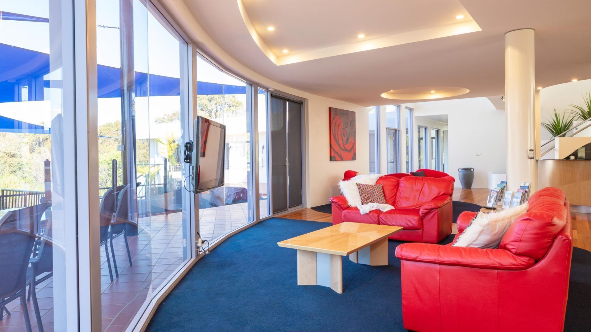 A modern living room with a red sofa, a coffee table, and a TV mounted on a glass wall.