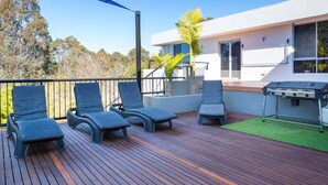 Een terras met loungezetels, een barbecue en een modern huis op de achtergrond.
