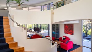 Een modern interieur met een gebogen trap, een rode bank en een groot raam met uitzicht op de omgeving.