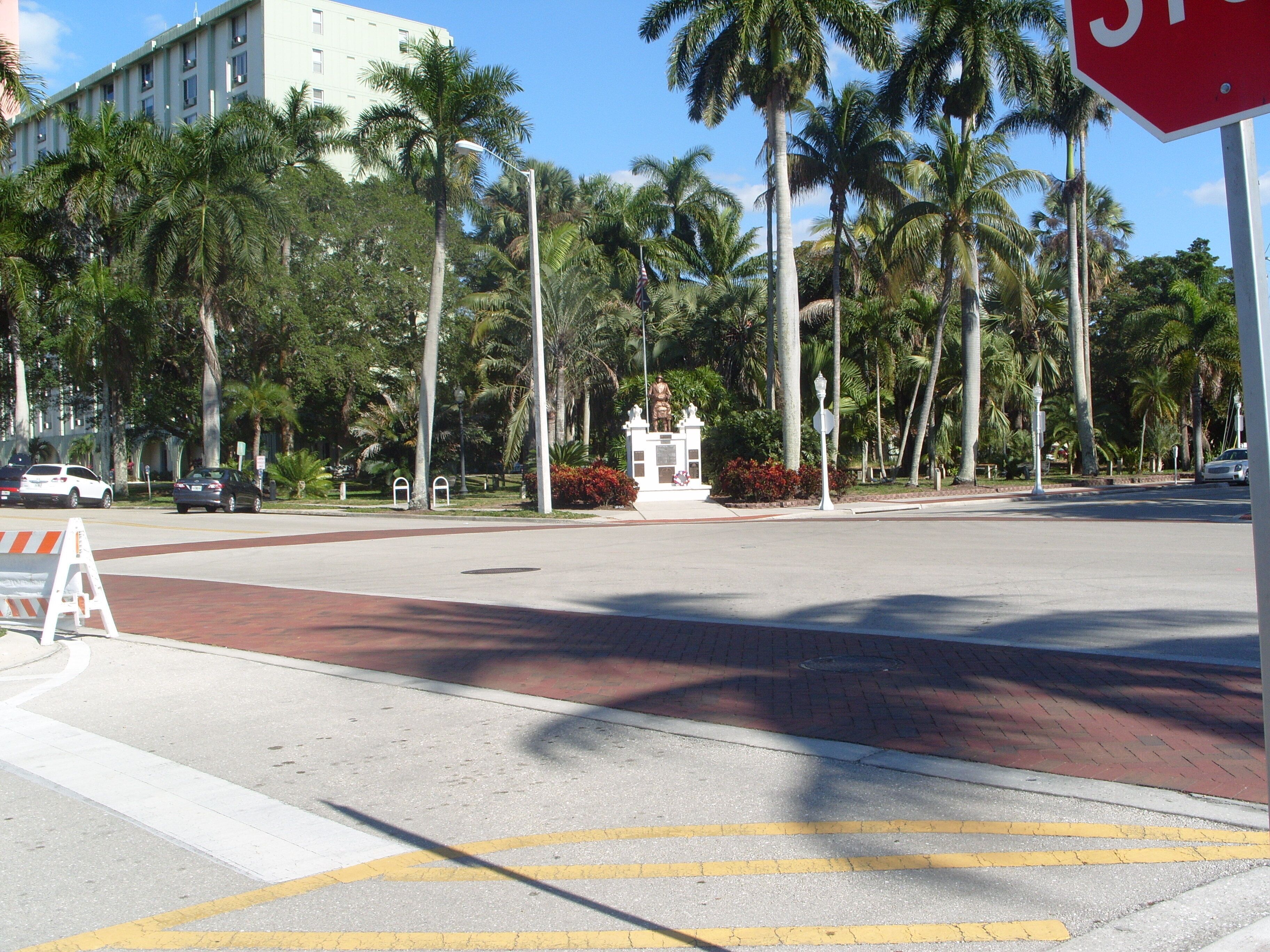Una intersección de calles con palmeras, una señal de alto y una estatua en el centro.