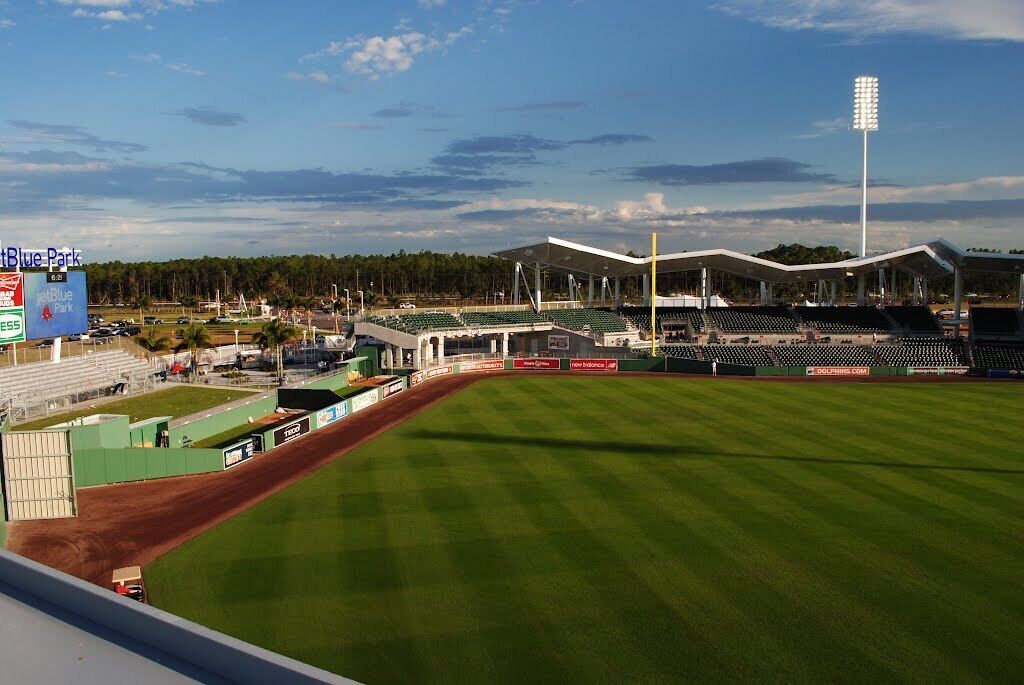 A baseball stadium with a green field, seating areas, and a large scoreboard.