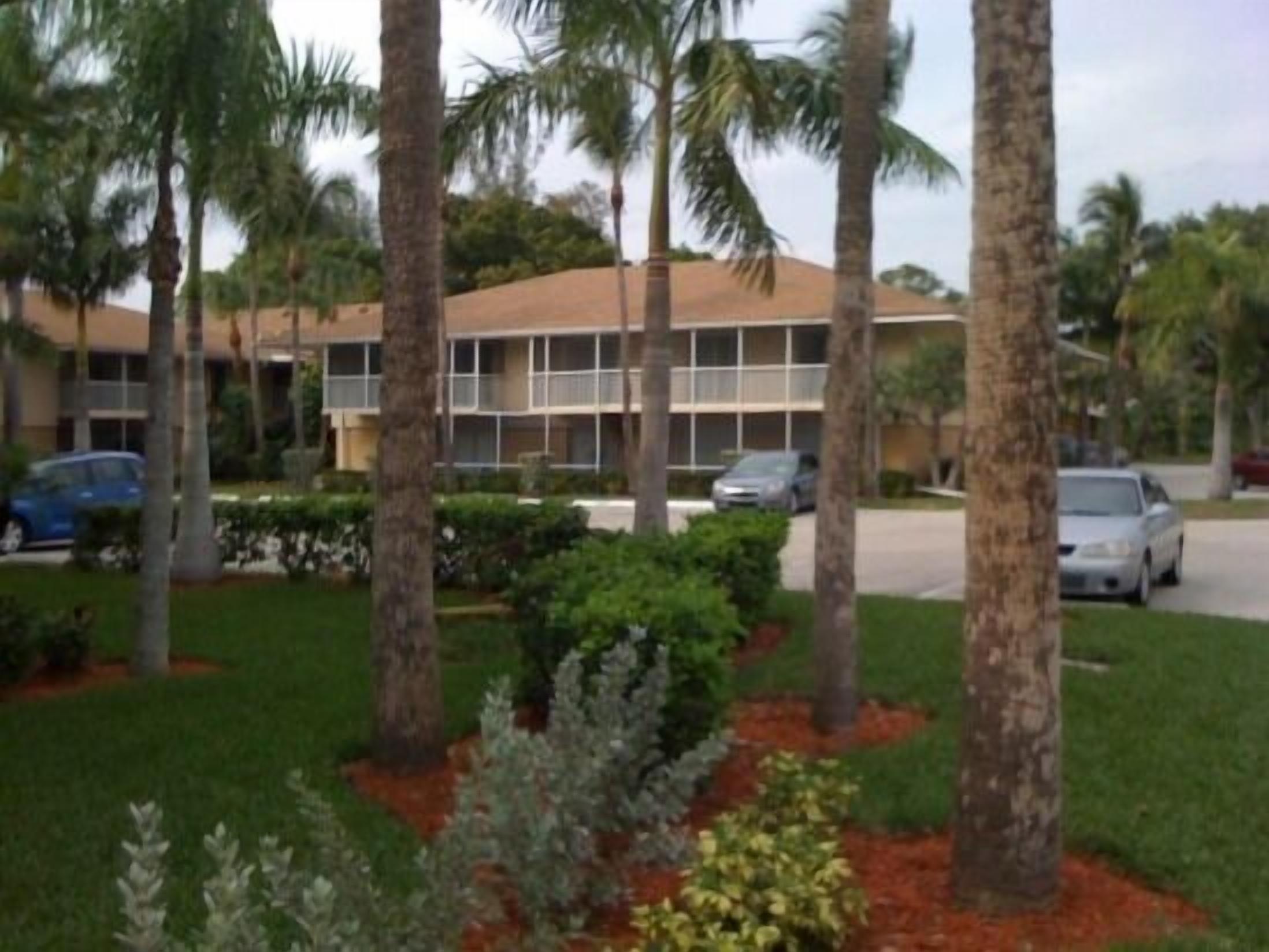 A building with a flat roof and multiple windows, surrounded by palm trees and a well-maintained lawn.