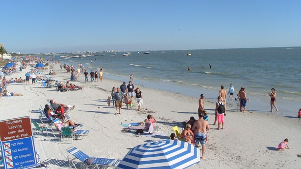 Ein voller Strand mit Menschen, die sich sonnen, schwimmen und am Ufer entlanggehen.